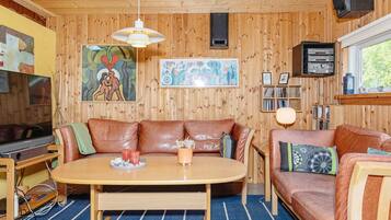 A cozy room with a wooden ceiling, a brown leather sofa, a wooden dining table, and a television.