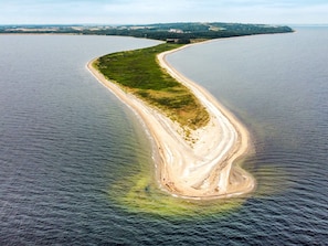 An aerial view of a curving coastline with a sandy beach and a small island with greenery. - 6 Person Holiday Home in Fur (Fur)
