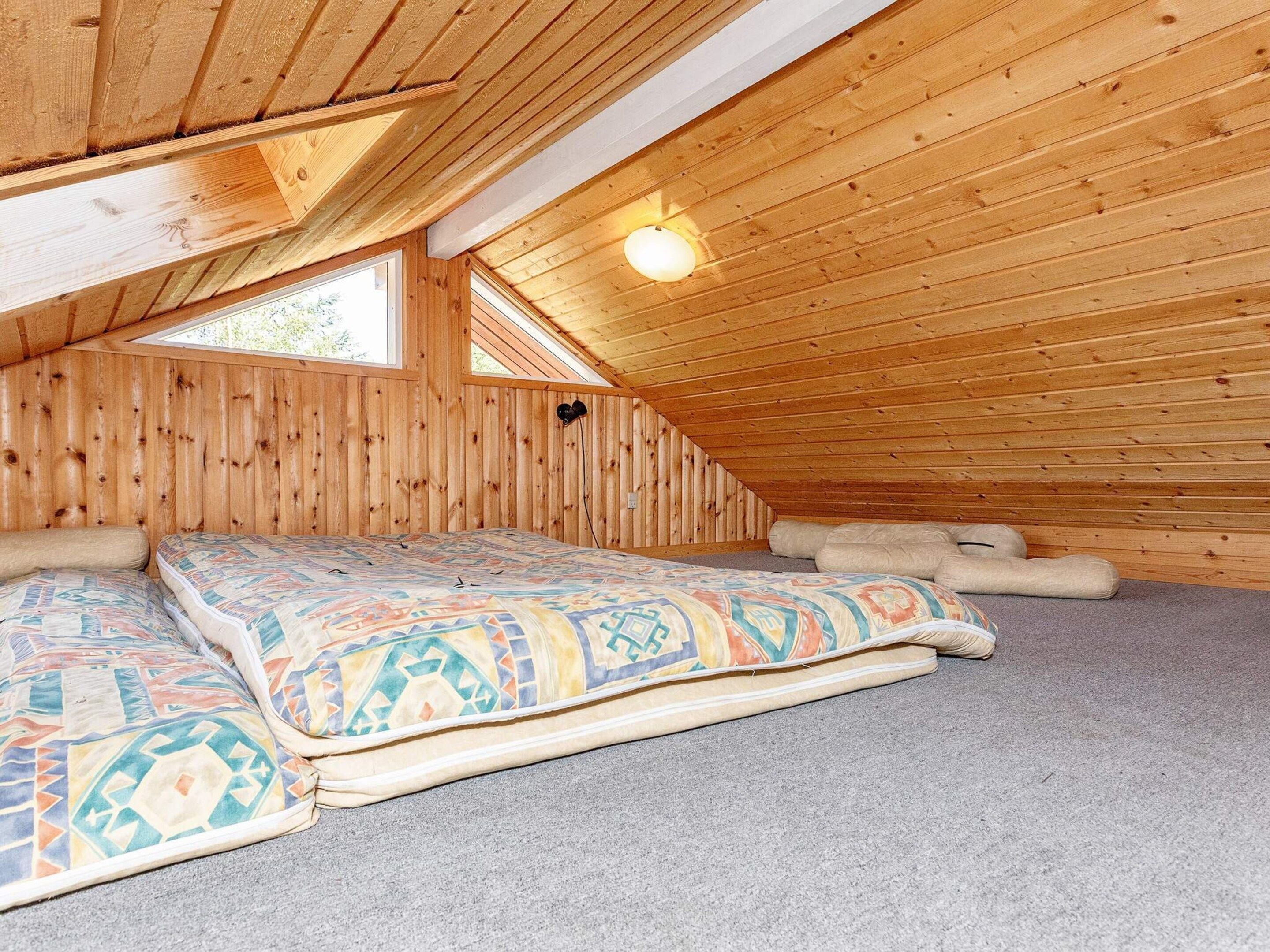 A cozy attic bedroom with a sloped ceiling, a bed with patterned bedding, and a single wall-mounted light fixture.