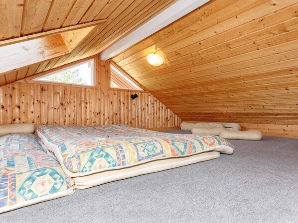 Un dormitorio acogedor en el ático con techo inclinado, cama con ropa de cama estampada y una lámpara de pared sencilla.