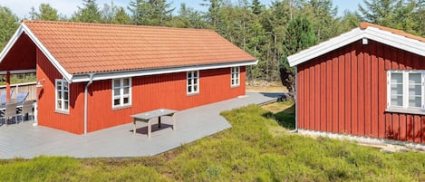 A red wooden cabin with a covered patio and a separate small building.
