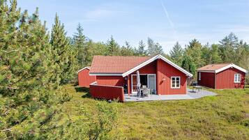 A red wooden cabin with a covered patio, surrounded by dense forest.