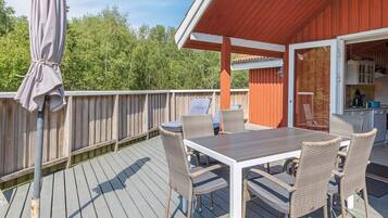 A covered outdoor deck with a dining table and chairs, a grill, and a view of the surrounding trees.