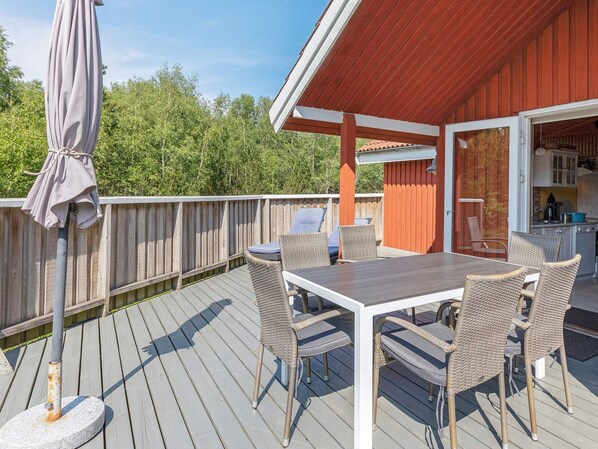A covered outdoor deck with a dining table and chairs, a grill, and a view of the surrounding trees.