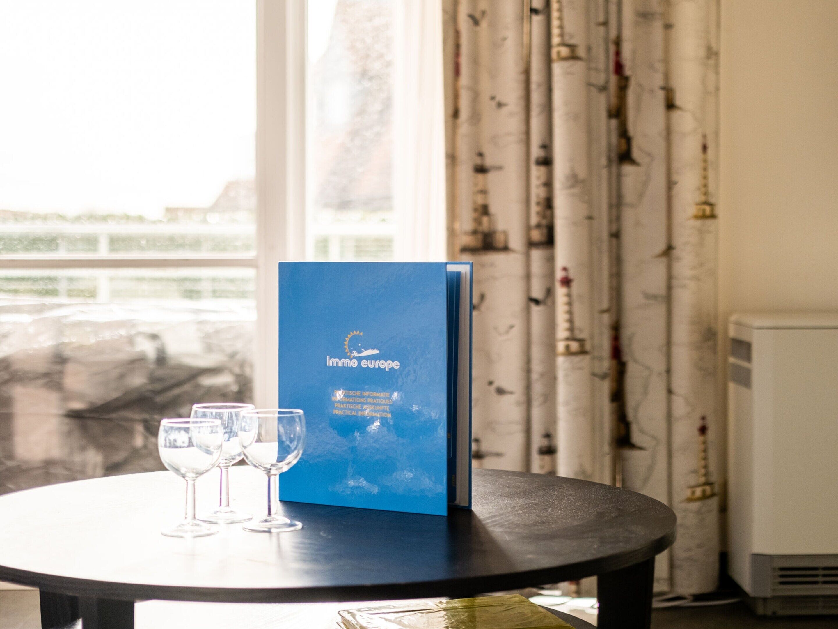 A table with a blue booklet titled 'immo europe' and two wine glasses.