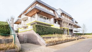 A multi-story residential building with a prominent staircase leading to the entrance, a balcony on the second floor, and a well-maintained hedge in front. - Apartment Near Koksijde Beach With Terrace (Koksijde)