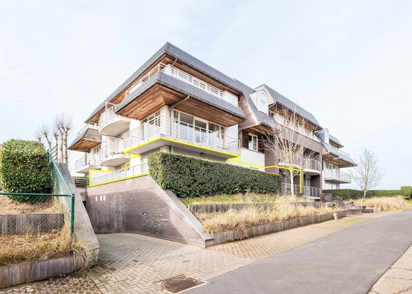 A modern multi-story house with a prominent balcony, a sloped roof, and a landscaped front yard. - Apartment Near Koksijde Beach With Terrace (Koksijde)