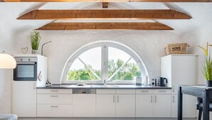 A modern kitchen with white cabinets, a large arched window, and wooden beams on the ceiling. - No. 7 Lake View Modern Retreat (Aurich)