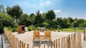 A sandy outdoor area with two wooden chairs, a small wooden structure, and a fenced playground. - No. 7 Lake View Modern Retreat (Aurich)
