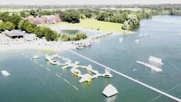 An aerial view of a lakeside property with boats, a dock, and a building with a red roof. - No. 7 Lake View Modern Retreat (Aurich)
