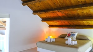 A bedroom with a wooden ceiling, a bed with a beige mattress, and a bedside table with rolled towels.