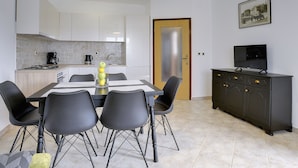 A modern kitchen with white cabinets, a dining table with chairs, a coffee maker, and a television on a cabinet. - Nicely Decorated Apartment With Private Pool (Vodnjan)
