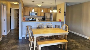 A modern kitchen with wooden cabinets, a stainless steel refrigerator, and a built-in microwave. There is a dining area with a wooden table and chairs, and a small island with bar stools. - 1st floor, FP, mtn & pond view, deck, pool, pet-friendly. F1663 by LRS (Lincoln)