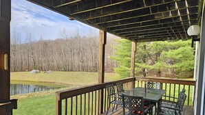 A wooden deck with a table and chairs, overlooking a pond and a forested area. - 1st floor, FP, mtn & pond view, deck, pool, pet-friendly. F1663 by LRS (Lincoln)