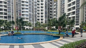 A swimming pool surrounded by a landscaped area with palm trees and a high-rise building in the background. - JB City DangaBay Shopping Mall Apartment (Johor Bahru)