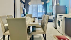 A modern kitchen with a built-in washing machine, a dining area with a long table and chairs, and a large window with curtains. - JB City DangaBay Shopping Mall Apartment (Johor Bahru)