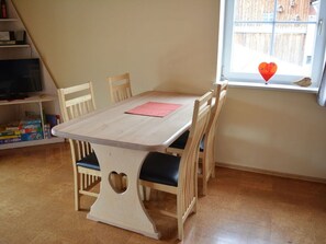 A wooden dining table with chairs, a heart-shaped cutout on the table, and a window with a view of a wooden fence. - Holiday Apartment Schiechtele 2 (Pfronten)
