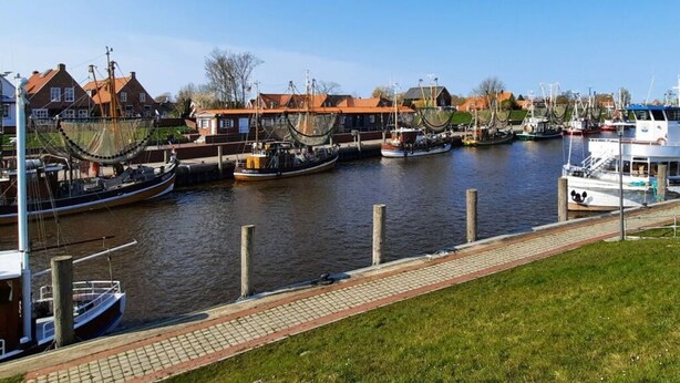 A marina with several boats docked, a grassy area in the foreground, and buildings with red roofs in the background. - Luetje Huuske Modern Retreat (Krummhoern)