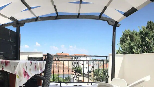Un espacio al aire libre cubierto con una mesa y sillas, y una vista de edificios y árboles al fondo.