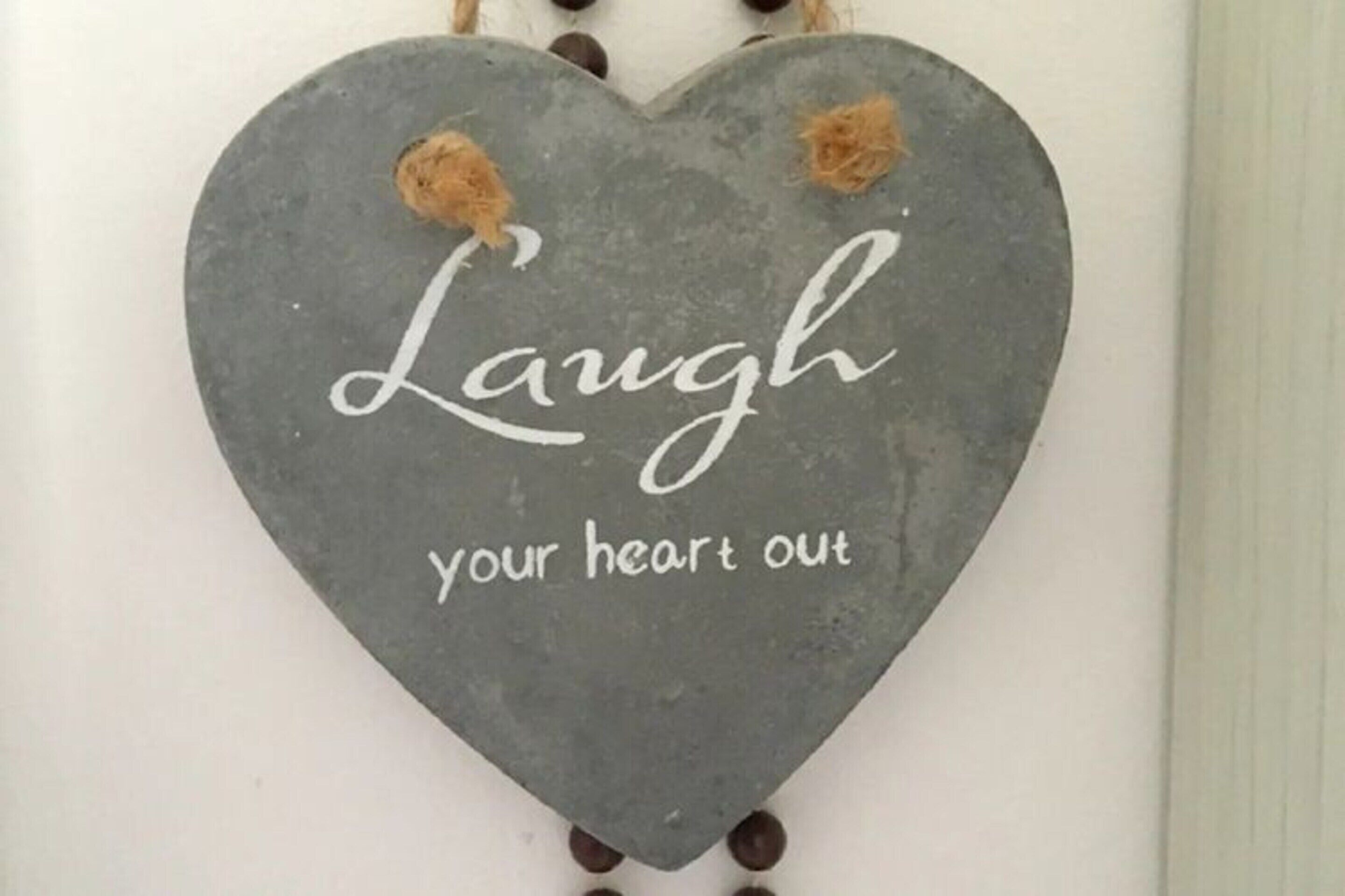 A heart-shaped sign with the text "Laugh your heart out" on a wall.