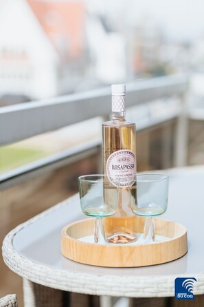 Eine Flasche Roséwein und zwei Gläser auf einem runden Holztablett auf einem Balkontisch.