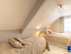 Ein modernes Schlafzimmer mit zwei Betten, einer geneigten Decke und einem Fenster mit Vorhängen.