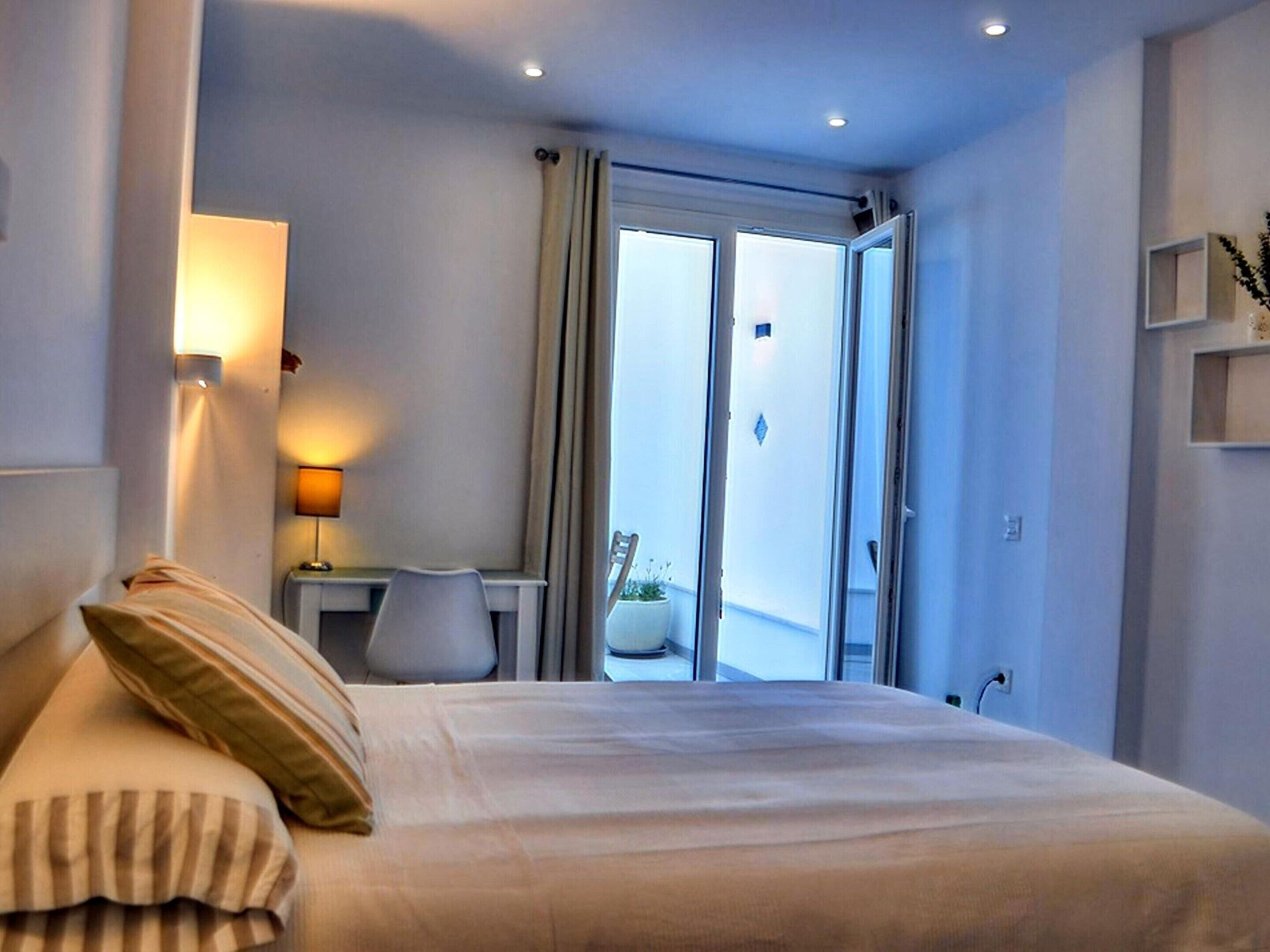 A hotel room with a bed, a desk, a lamp, and a view of the outdoors through a sliding door.