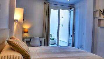A hotel room with a bed, a desk, a lamp, and a view of the outdoors through a sliding door.