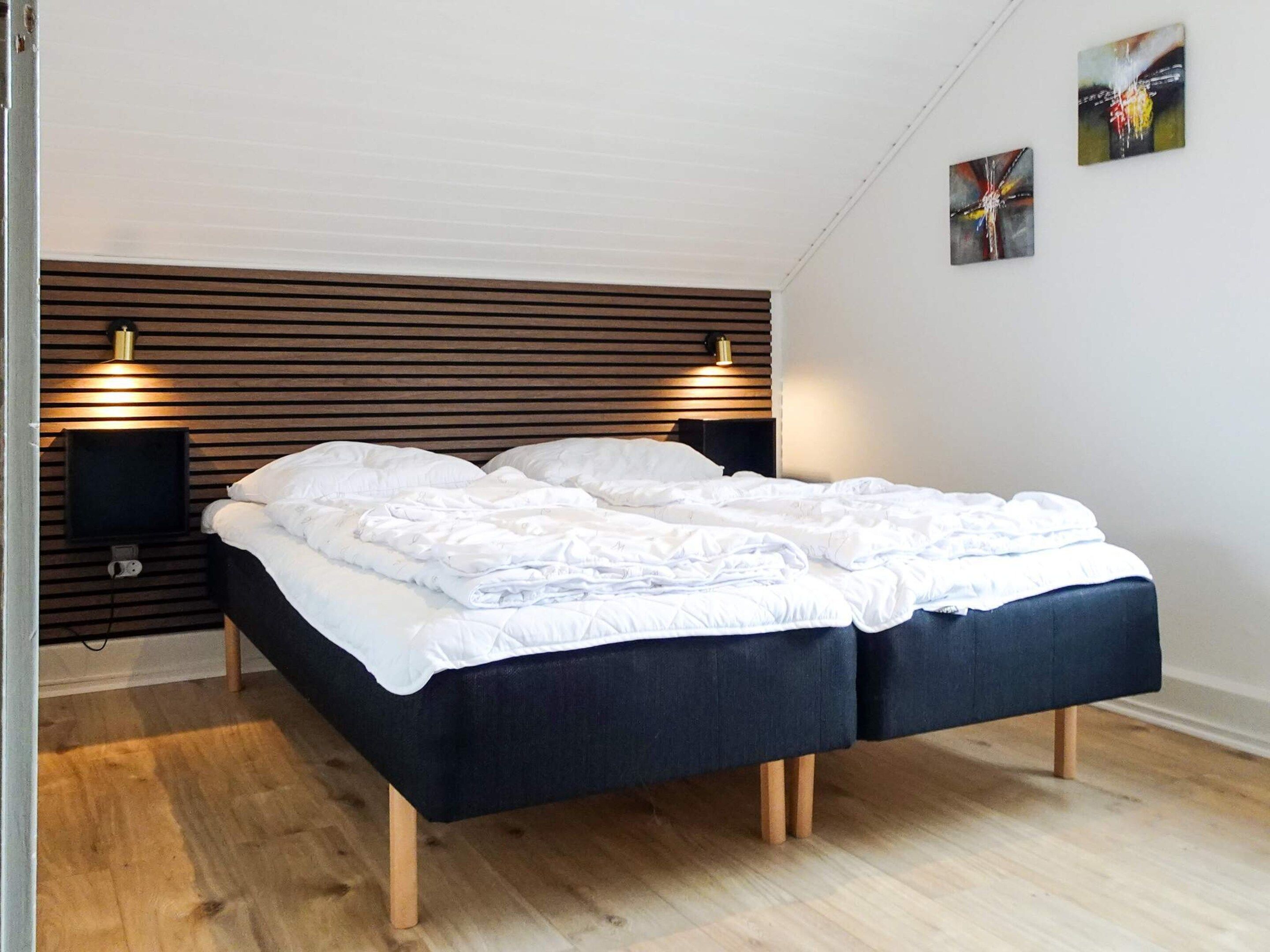 Une chambre moderne avec une tête de lit en lattes de bois, deux tables de chevet avec des lampes, un téléviseur à écran plat et un grand lit avec une literie blanche.