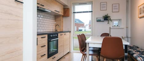 Une cuisine moderne avec des meubles en bois, une cuisinière noire et un coin repas comprenant une table et des chaises.