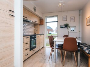Een moderne keuken met houten kastjes, een zwarte kookplaat en een eethoek met een tafel en stoelen.