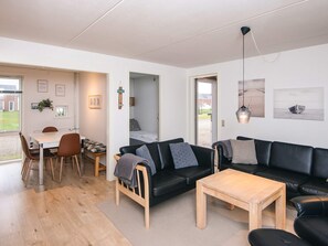 Een moderne woonkamer met een zwarte leren bank, een houten salontafel en een eethoek met een witte tafel en stoelen.