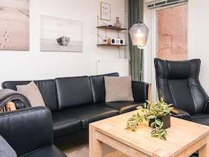 A modern living room with a black leather sofa, a wooden coffee table, and a black leather armchair.
