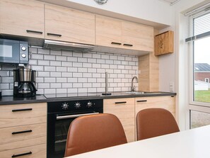 A modern kitchen with light wood cabinets, a black countertop, a stainless steel range hood, a coffee maker, and a window with a view of a building.