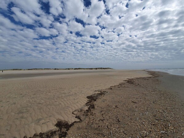 A wide sandy beach with a gentle slope leading to the sea, under a partly cloudy sky.