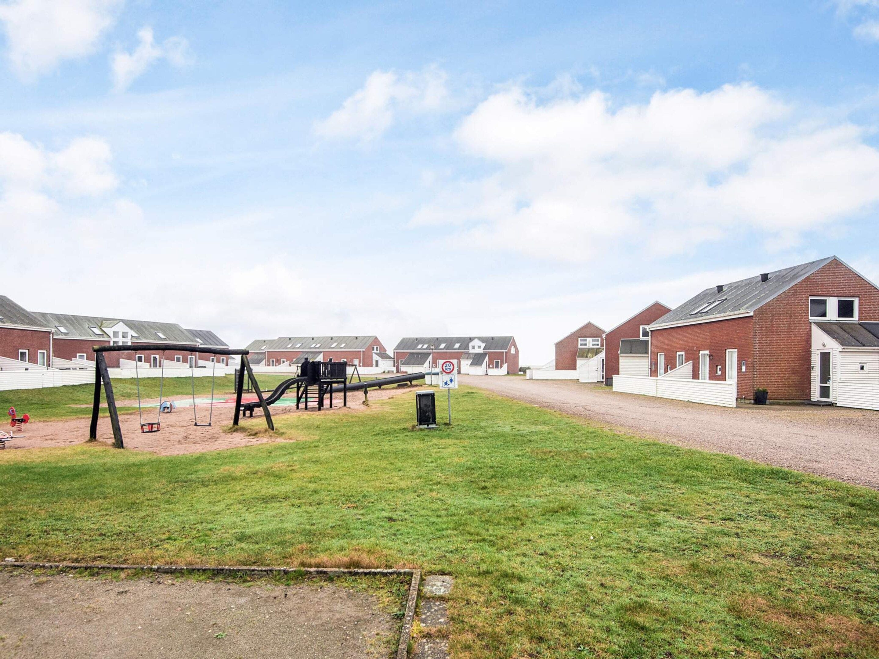 A playground with swings and slides, surrounded by brick buildings with flat roofs.