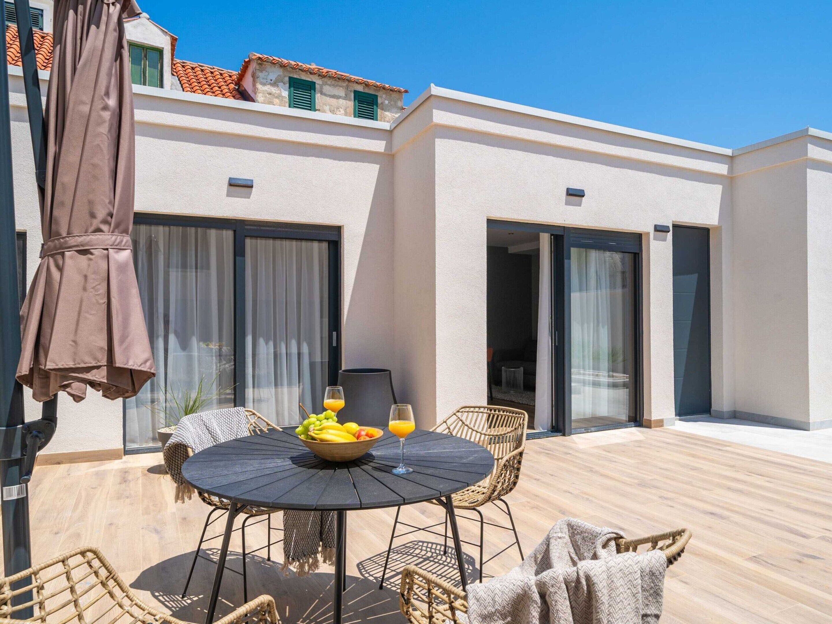 A patio with a round table, wicker chairs, a bowl of fruit, and a glass of orange juice.