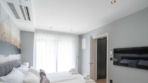 A modern bedroom with a large bed, a flat-screen TV, and a large window with sheer curtains. - Apartments Villa Royale - Luxury One Bedroom Apartment With Terrace (Konavle)