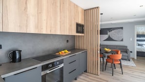 A modern kitchen with wooden cabinets, a built-in oven, and a dining area with a table and chairs. - Apartments Villa Royale - Luxury One Bedroom Apartment With Terrace (Konavle)