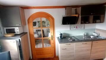 Eine kleine Küche mit Holztür, einer Mikrowelle, einem Spülbecken und einem kleinen Kühlschrank.