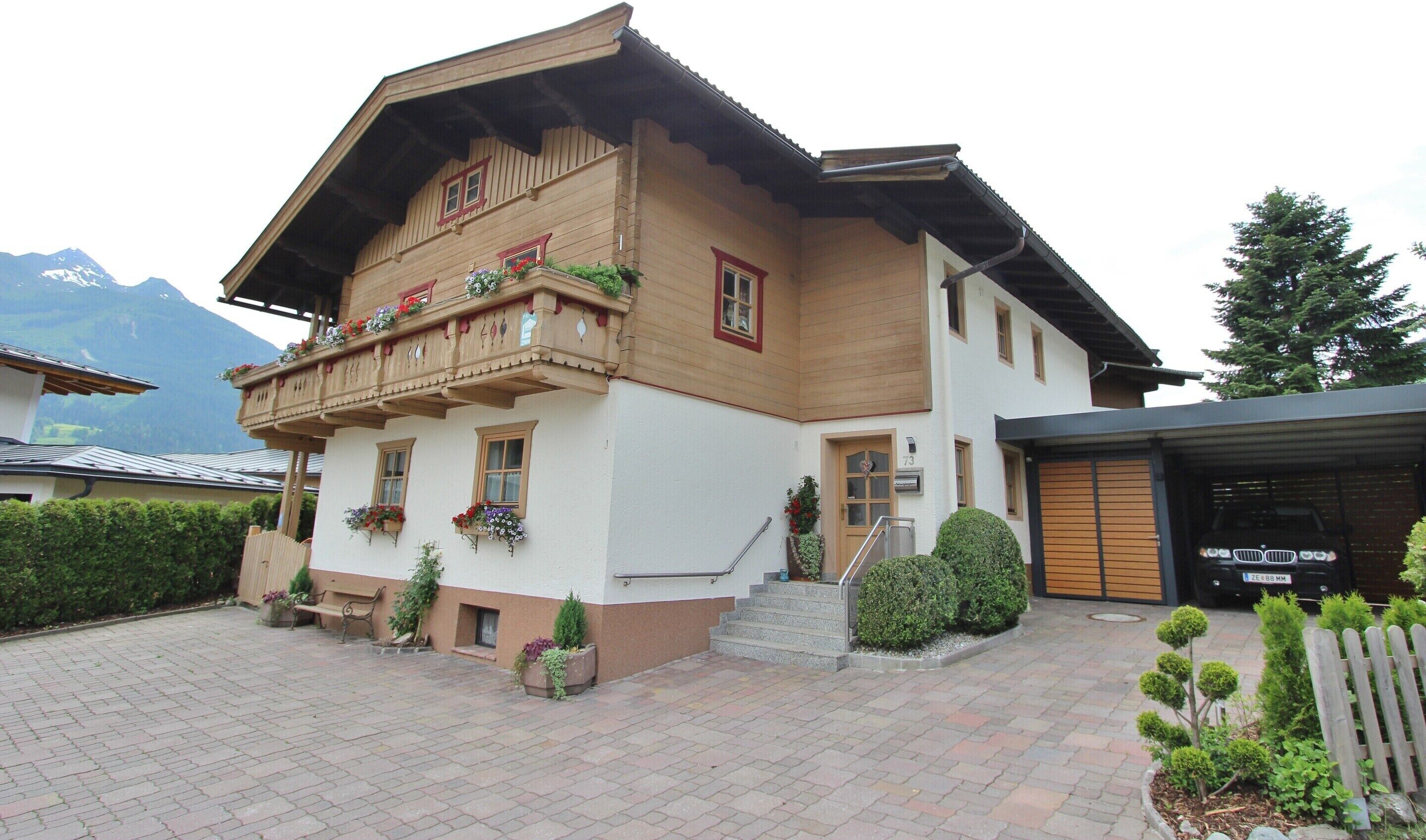 A two-story building with a balcony, a garage, and a mountain backdrop.