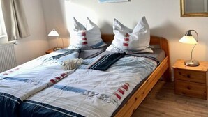 Siististi pedattu sänky, jossa on sinivalkoinen peitto, kaksi yöpöytävalaisinta, puinen yöpöytä, peili ja taulu seinällä.