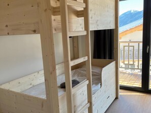 A wooden bunk bed with a ladder, a window with a view of a balcony and mountains, and a door leading outside.