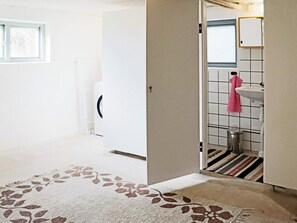 Een kamer met een groot raam, een wasmachine, een wastafel met een roze handdoek en een kamerbreed tapijt met dessin.