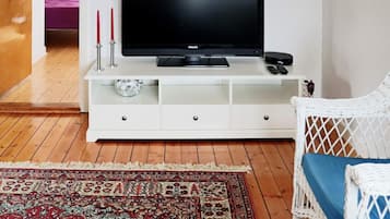Una sala de estar con un mueble blanco para entretenimiento, un televisor de pantalla plana, un sillón de mimbre y una alfombra estampada.