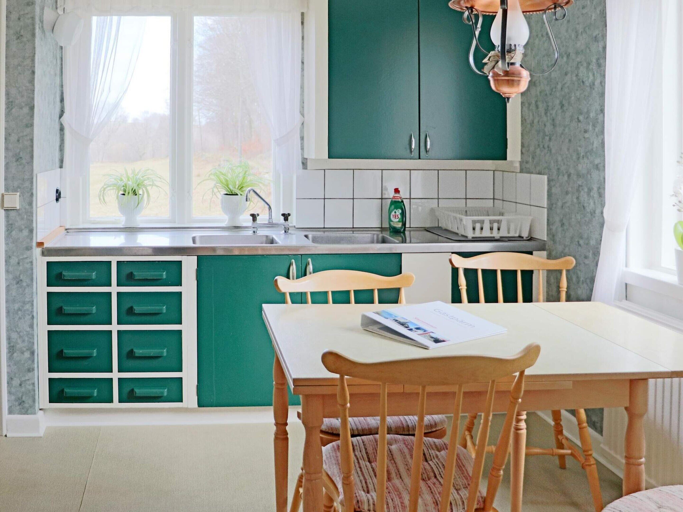 A kitchen with green cabinets, a white countertop, and a window with sheer curtains.