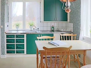 Et køkken med grønne skabe, en hvid bordplade og et vindue med let gardin.