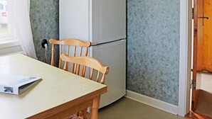 A room with a wooden chair, a white refrigerator, and a table with a magazine. - 9 Person Holiday Home in Bastad (Bastad)