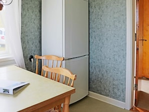 Une pièce avec une chaise en bois, un réfrigérateur blanc et une table sur laquelle se trouve un magazine.