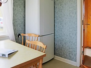 Een kleine keuken met een houten stoel, een tafel en een koelkast.